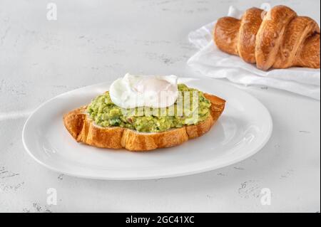 Croissant avec guacamole et œuf poché sur l'assiette de service Banque D'Images