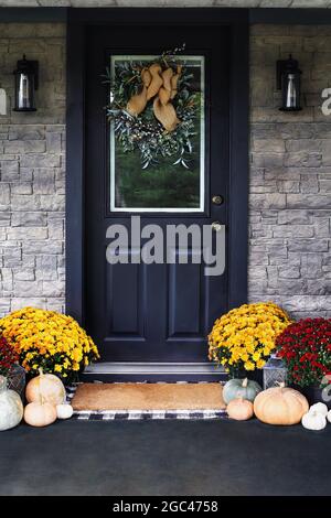 Porche avant décoré pour le jour de Thanksgiving avec couronne maison accrochée à la porte. Gourdes, citrouilles blanches, vertes et orange et mamans colorées Banque D'Images