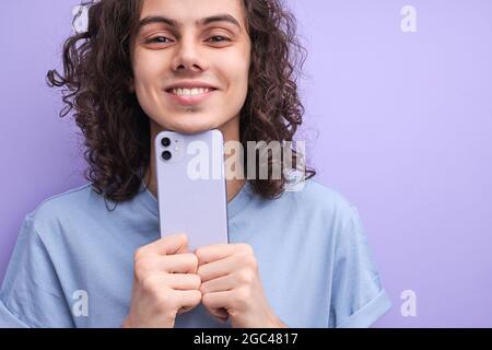 Joyeux adolescent caucasien avec des cheveux bouclés , tenant smartphone, regardant enthousiaste, écran de gadget, enregistrer vidéo, assistez à un événement amusant et prenez des photos Banque D'Images