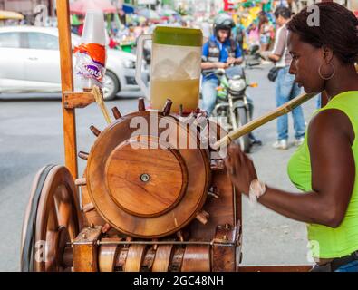 CALI, COLOMBIE - 9 SEPTEMBRE 2015 : une femme presse le jus de canne à sucre à l'aide d'une vieille machine en bois dans une rue du centre de Cali. Banque D'Images