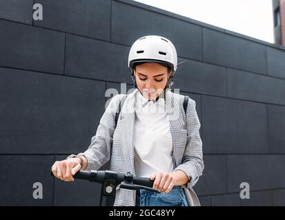 Jeune femme caucasienne portant un casque blanc de cyclisme tenant le guidon du scooter électrique Banque D'Images