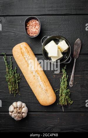 Ensemble composé de pain à l'ail, beurre et ingrédients aux herbes, sur fond de table en bois noir, dessus de lit plat Banque D'Images