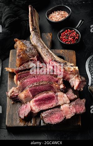 Barbecue traditionnel, set de tranches de steak de tomahawk de Wagyu vieilli sec, sur un plateau de service en bois, sur fond de pierre noire Banque D'Images