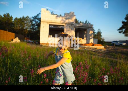 Une petite fille joue et danse près du chantier de construction de sa future maison à la campagne. En attente d'un déménagement, rêves de logements futurs. Mortga Banque D'Images