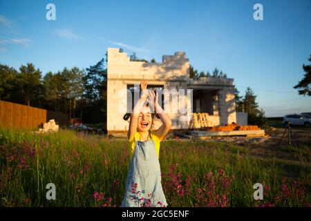 Une petite fille joue et danse près du chantier de construction de sa future maison à la campagne. En attente d'un déménagement, rêves de logements futurs. Mortga Banque D'Images