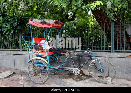 Vue d'un pauvre homme qui dormait dans son pousse-pousse à vélo pendant qu'il prend une pause entre ses voyages. Banque D'Images