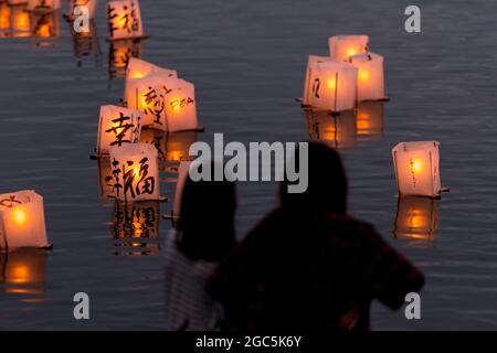 Seattle, États-Unis. 6 août 2021. Au crépuscule, les gens regardent les lanternes flottantes en papier de riz au mémorial du 76e anniversaire de Hiroshima à Hope. Les gens se rassemblent chaque année sur les rives du lac Green, juste au nord du centre-ville de Seattle, ils éclairent les lanternes en papier de riz avec des bougies dans les mémoires des victimes de l'attentat à la bombe nucléaire d'Hiroshima pendant la deuxième Guerre mondiale. Crédit : James Anderson/Alay Banque D'Images