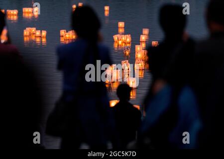 Seattle, États-Unis. 6 août 2021. Au crépuscule, les gens regardent les lanternes flottantes en papier de riz au mémorial du 76e anniversaire de Hiroshima à Hope. Les gens se rassemblent chaque année sur les rives du lac Green, juste au nord du centre-ville de Seattle, ils éclairent les lanternes en papier de riz avec des bougies dans les mémoires des victimes de l'attentat à la bombe nucléaire d'Hiroshima pendant la deuxième Guerre mondiale. Crédit : James Anderson/Alay Banque D'Images