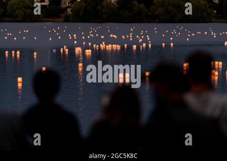 Seattle, États-Unis. 6 août 2021. Au crépuscule, les gens regardent les lanternes flottantes en papier de riz au mémorial du 76e anniversaire de Hiroshima à Hope. Les gens se rassemblent chaque année sur les rives du lac Green, juste au nord du centre-ville de Seattle, ils éclairent les lanternes en papier de riz avec des bougies dans les mémoires des victimes de l'attentat à la bombe nucléaire d'Hiroshima pendant la deuxième Guerre mondiale. Crédit : James Anderson/Alay Banque D'Images