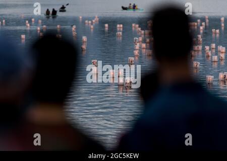 Seattle, États-Unis. 6 août 2021. Au crépuscule, les gens regardent les lanternes flottantes en papier de riz au mémorial du 76e anniversaire de Hiroshima à Hope. Les gens se rassemblent chaque année sur les rives du lac Green, juste au nord du centre-ville de Seattle, ils éclairent les lanternes en papier de riz avec des bougies dans les mémoires des victimes de l'attentat à la bombe nucléaire d'Hiroshima pendant la deuxième Guerre mondiale. Crédit : James Anderson/Alay Banque D'Images