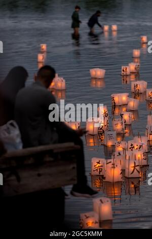 Seattle, États-Unis. 6 août 2021. Au crépuscule, les gens regardent les lanternes flottantes en papier de riz au mémorial du 76e anniversaire de Hiroshima à Hope. Les gens se rassemblent chaque année sur les rives du lac Green, juste au nord du centre-ville de Seattle, ils éclairent les lanternes en papier de riz avec des bougies dans les mémoires des victimes de l'attentat à la bombe nucléaire d'Hiroshima pendant la deuxième Guerre mondiale. Crédit : James Anderson/Alay Banque D'Images