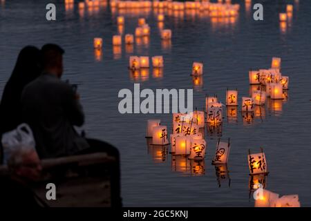 Seattle, États-Unis. 6 août 2021. Au crépuscule, les gens regardent les lanternes flottantes en papier de riz au mémorial du 76e anniversaire de Hiroshima à Hope. Les gens se rassemblent chaque année sur les rives du lac Green, juste au nord du centre-ville de Seattle, ils éclairent les lanternes en papier de riz avec des bougies dans les mémoires des victimes de l'attentat à la bombe nucléaire d'Hiroshima pendant la deuxième Guerre mondiale. Crédit : James Anderson/Alay Banque D'Images