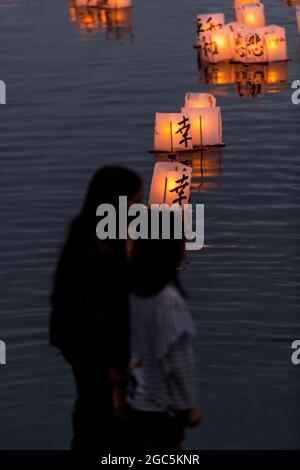 Seattle, États-Unis. 6 août 2021. Au crépuscule, les gens regardent les lanternes flottantes en papier de riz au mémorial du 76e anniversaire de Hiroshima à Hope. Les gens se rassemblent chaque année sur les rives du lac Green, juste au nord du centre-ville de Seattle, ils éclairent les lanternes en papier de riz avec des bougies dans les mémoires des victimes de l'attentat à la bombe nucléaire d'Hiroshima pendant la deuxième Guerre mondiale. Crédit : James Anderson/Alay Banque D'Images