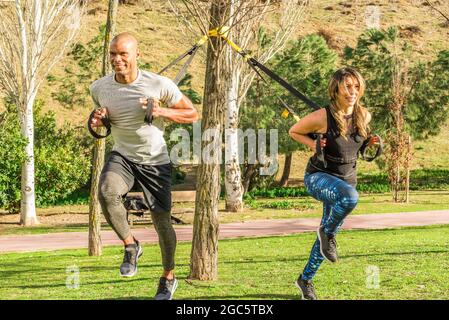 Couple de forme physique faisant de l'exercice de jambes de dos avec des sangles de forme physique dans le parc Banque D'Images