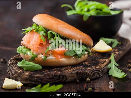 Sandwich frais avec saumon et bagel, roquette sauvage dans un bol noir et fromage à la crème sur bois avec citron et poivre. Banque D'Images