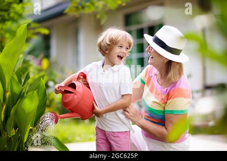 Jardinage de femme et d'enfant. Grand-mère et petit garçon au soleil chapeau arroser les plantes et les fleurs du jardin. Les enfants travaillent dans une belle cour ensoleillée en pleine floraison. Banque D'Images