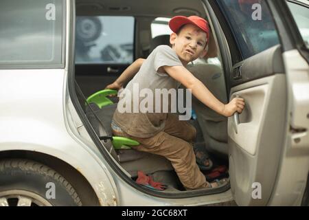 L'enfant sort de la voiture. Le garçon est arrivé dans le véhicule. L'enfant a ouvert la porte arrière de la voiture. Banque D'Images