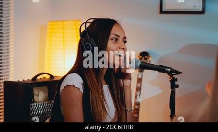 Chanteuse noire féminine en casque enregistrant sa nouvelle chanson en studio à domicile, chantant sensuellement dans le microphone Banque D'Images