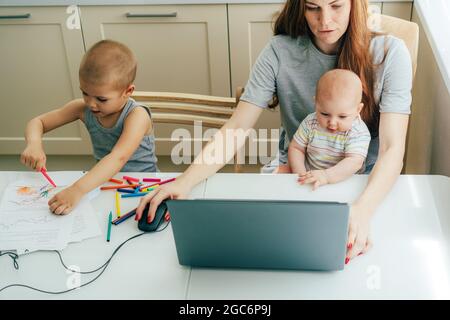 Une femme d'affaires occupée avec un bébé dans ses bras travaille sur un ordinateur portable, à côté d'un bébé tire. Banque D'Images