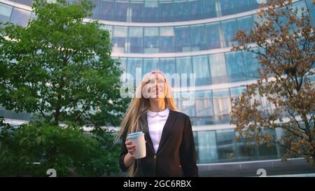 Par en dessous de la blonde woman in suit le café dans la tasse de papier à l'écart sur rue. Banque D'Images