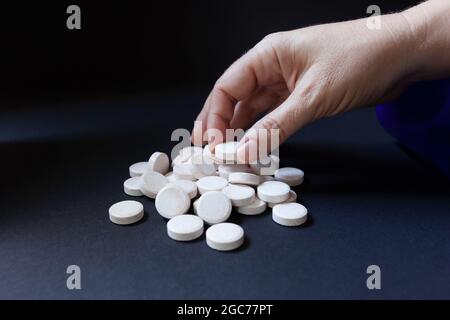 La main de la femme ramassant l'une des nombreuses pilules blanches sur fond sombre Banque D'Images