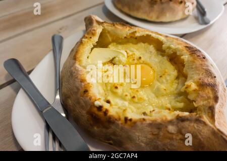 Khachapuri cuisine géorgienne traditionnelle Adjara repas sur une assiette dans un restaurant. Gros plan sur du pain cuit avec du fromage et des œufs Banque D'Images