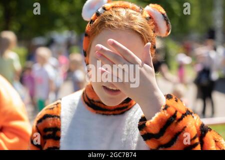 La fille ferme les yeux avec sa main. Un adolescent en pyjama tigre. La fille ne veut pas regarder. Animateur pour enfants en vacances. Banque D'Images