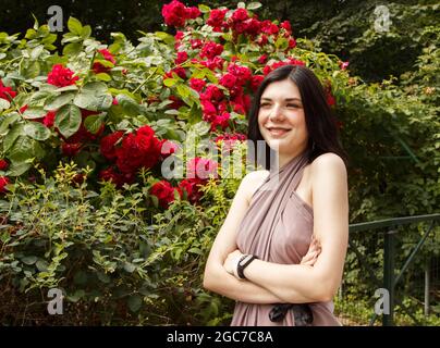 portrait d'une jeune femme brune debout près d'une roseraie le jour de l'été. gros plan extérieur Banque D'Images