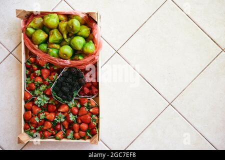 Le kit avec des boîtes de fraises, framboises, figues et mûres se trouve sur un carreau léger Banque D'Images