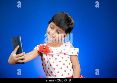 Petite fille enfant ou tout-petit prenant selfie et de vérifier des photos de téléphone mobile sur fond bleu - concept de la technologie, Internet et moderne Banque D'Images