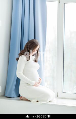 Femme enceinte gaie assise près de la fenêtre Banque D'Images