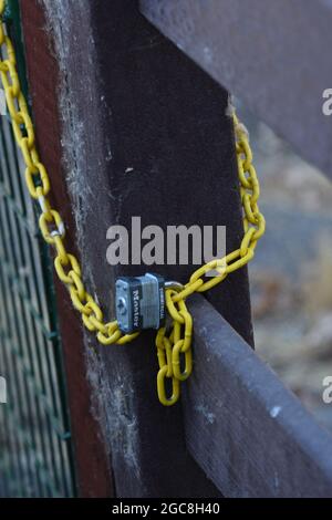 Un cadenas bloquant l'entrée d'une route privée sur une ferme où ils veulent que les autres restent à l'extérieur et voient la chaîne jaune autour de la porte et la zone clôturée Banque D'Images