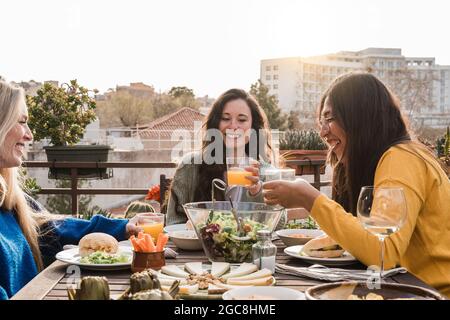 Des amis heureux mangeant de la nourriture végétalienne avec du jus à l'extérieur au restaurant patio - Focus sur le visage de femme africaine Banque D'Images