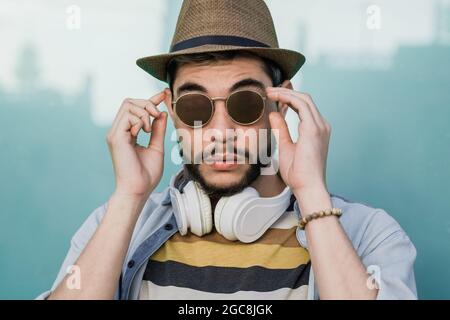 Jeune homme hippster regardant l'appareil photo extérieur portant des écouteurs pendant les vacances d'été - Focus sur le visage Banque D'Images