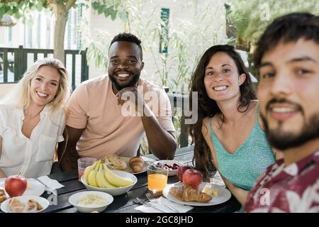 Les gens multiraciaux font un petit déjeuner pique-nique sain à la maison de ferme de campagne - heureux amis ayant plaisir à manger en plein air - Focus sur le visage de l'homme africain Banque D'Images