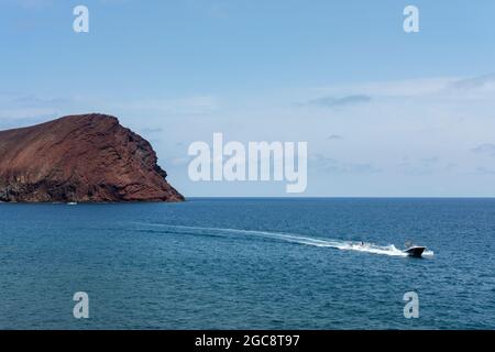 Traversée rapide en bateau à proximité de Montana Roja avec deux personnes qui se délissent derrière lui, vu de la promenade surélevée près de la plage, Playa la Tejita Banque D'Images