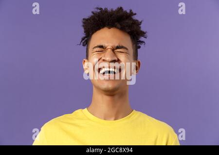 Gros plan portrait de jeune homme heureux et insouciant riant fort, chatoussant au-dessus de blague hilarante, se penchant vers l'arrière et les yeux proches tout en rigolant sur drôle Banque D'Images