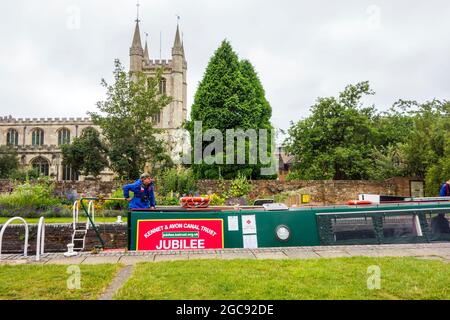 Kennet et Avon canal confiance narrowboat Jubilee passant par la ville Berkshire de Newbury avec l'église paroissiale de St Nicolas en arrière-plan Banque D'Images