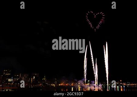 Feux d'artifice en forme de cœur sur les côtés d'un horizon urbain la nuit. D'autres feux d'artifice s'élèvent vers le cœur. Banque D'Images