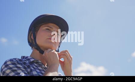 jeune femme cavalier ajuste la ceinture du casque avant de conduire. Photo de haute qualité Banque D'Images