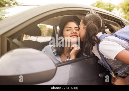 Petite fille dans un uniforme d'école et un sac à dos donnant à sa mère dans la voiture un baiser de Au revoir Banque D'Images