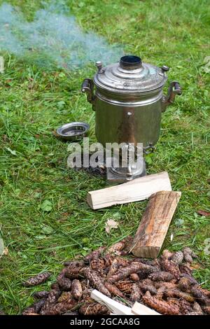 Chauffer le samovar avec des cônes pour faire du thé. Le samovar repose sur l'herbe. Fumée du tuyau Banque D'Images