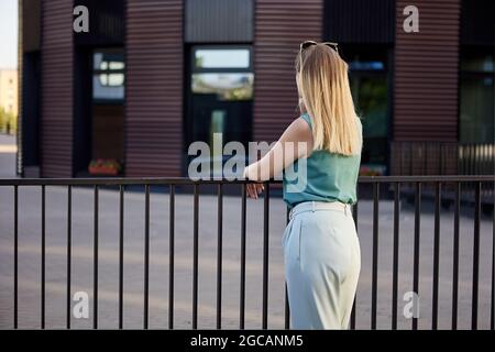 La femme mince se tient près de la clôture à l'extérieur pendant la journée. Banque D'Images