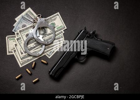 Crime et droit. Pistolet et balles 9 mm, menottes et billets en dollars américains sur fond noir. L'argent criminel et la punition, haut vi Banque D'Images