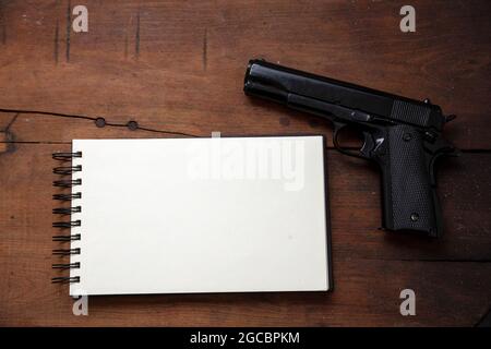 Note de suicide, concept de liste noire. Bloc-notes vierge et pistolet sur fond de table en bois, vue du dessus. Copier le modèle d'espace Banque D'Images