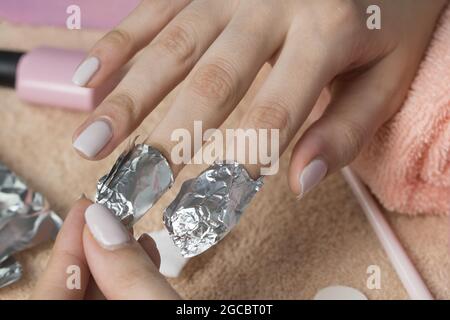 Retirez le produit à polir à base de gel avec du papier d'aluminium. La femme verse le liquide sur un tampon de coton, le met sur un clou et enveloppe le papier d'aluminium. Retrait des clous en shellac. Faites une manucure Banque D'Images