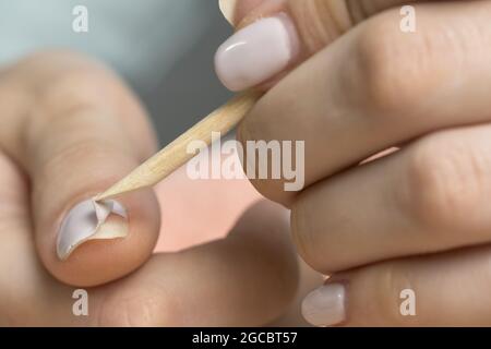 Retirer le gel à l'aide d'un bâton de bois. La femme retire le gel lustrant shellac des ongles à l'aide d'un poussoir, manucure à la maison. Retrait du gel polonais de na Banque D'Images