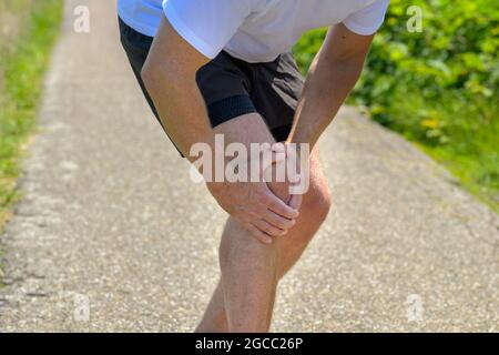 Un homme âgé embrassait le genou blessé dans une douleur après s'être blessé tout en faisant du jogging dans une vue rapprochée de l'articulation et de ses mains Banque D'Images