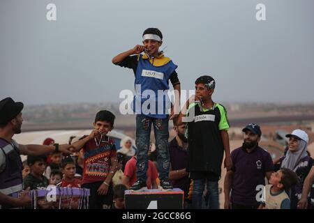 Idlib City, Syrie. 07e août 2021. Les enfants syriens célèbrent sur le podium avec des médailles symboliques distribuées parmi les gagnants d'une petite compétition olympique organisée pour les enfants déplacés par l'Organisation de secours et de développement Violet. L'événement sportif est organisé en conjonction avec les Jeux Olympiques de Tokyo en 2020 pour attirer l'attention sur les conditions dans les camps de réfugiés des personnes contraintes de se déplacer à l'intérieur du pays en raison du conflit civil en Syrie. Credit: Aras Alkharboutli/dpa/Alamy Live News Banque D'Images