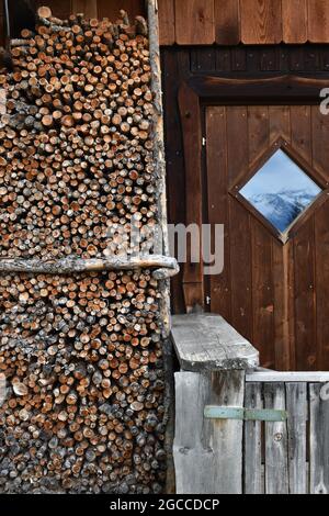 l'avant d'une cabine en bois avec une pile de bois et un reflet des montagnes environnantes dans la fenêtre de la porte au printemps de 2020 dans le tyrol oriental Banque D'Images